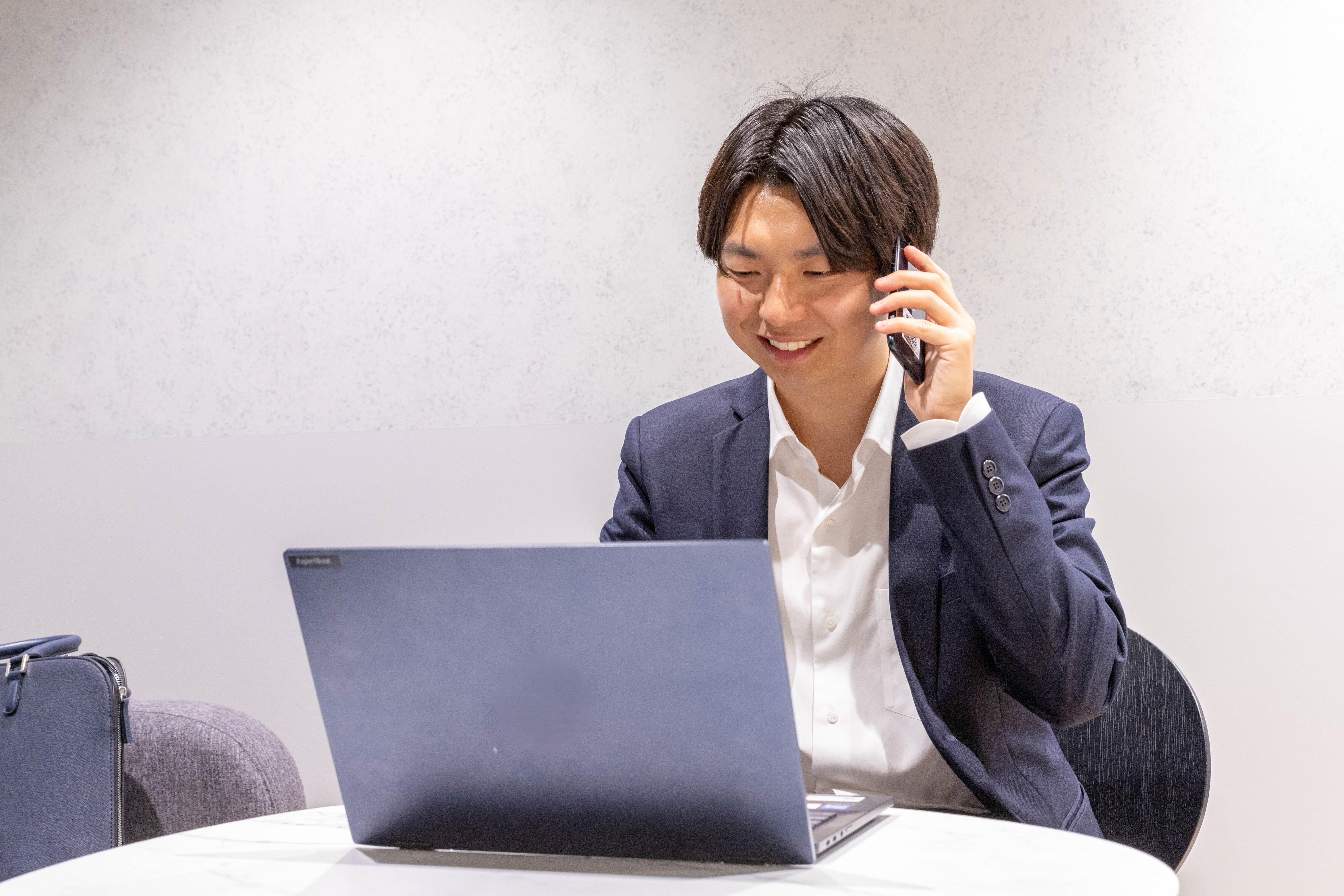 電話をかけながらPC作業をするスーツの男性